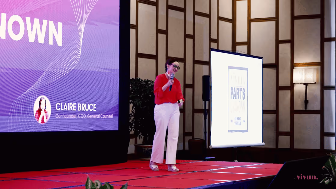 Speaker in red top presenting on stage with Parts slide behind her